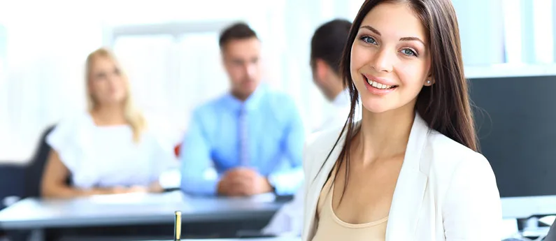 Confident young woman smiling in a professional setting with colleagues in the background