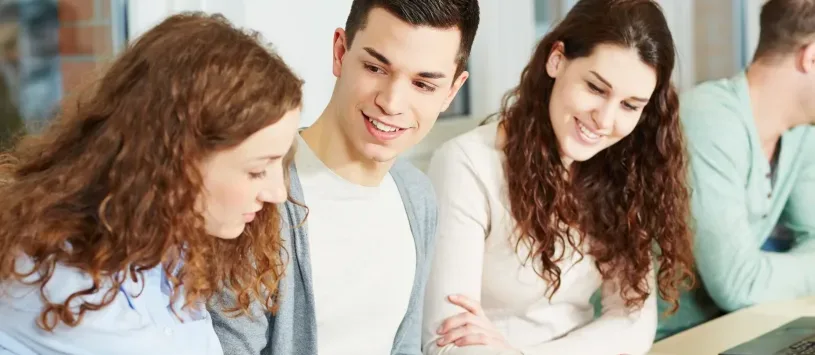 Students sitting together in a classroom, smiling and collaborating while taking notes.